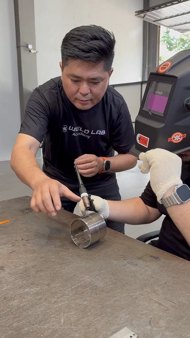 Massaru Oyama orientando a tocha na mão de um aluno sobre um tubo de inox