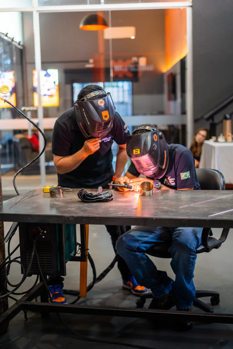 Dois soldadores de máscara trabalhando com TIG na bancada da Weldlab